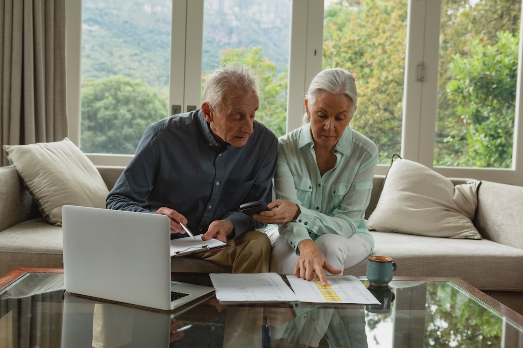 Couple assessing their finances on a laptop while sitting on a couch.
