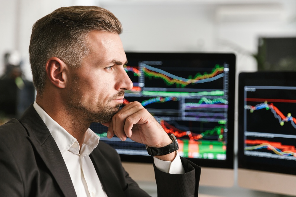 Man sitting at a desk in front of monitors displaying charts.