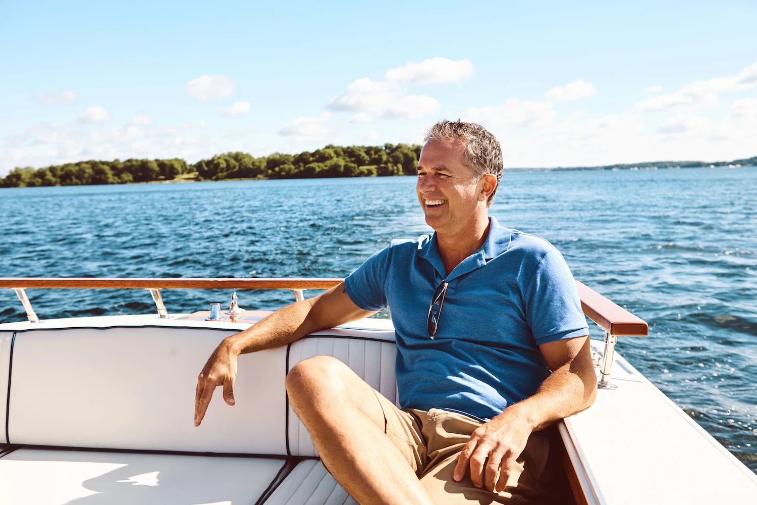 Smiling man in a blue button up shirt sitting on the bow of a boat.