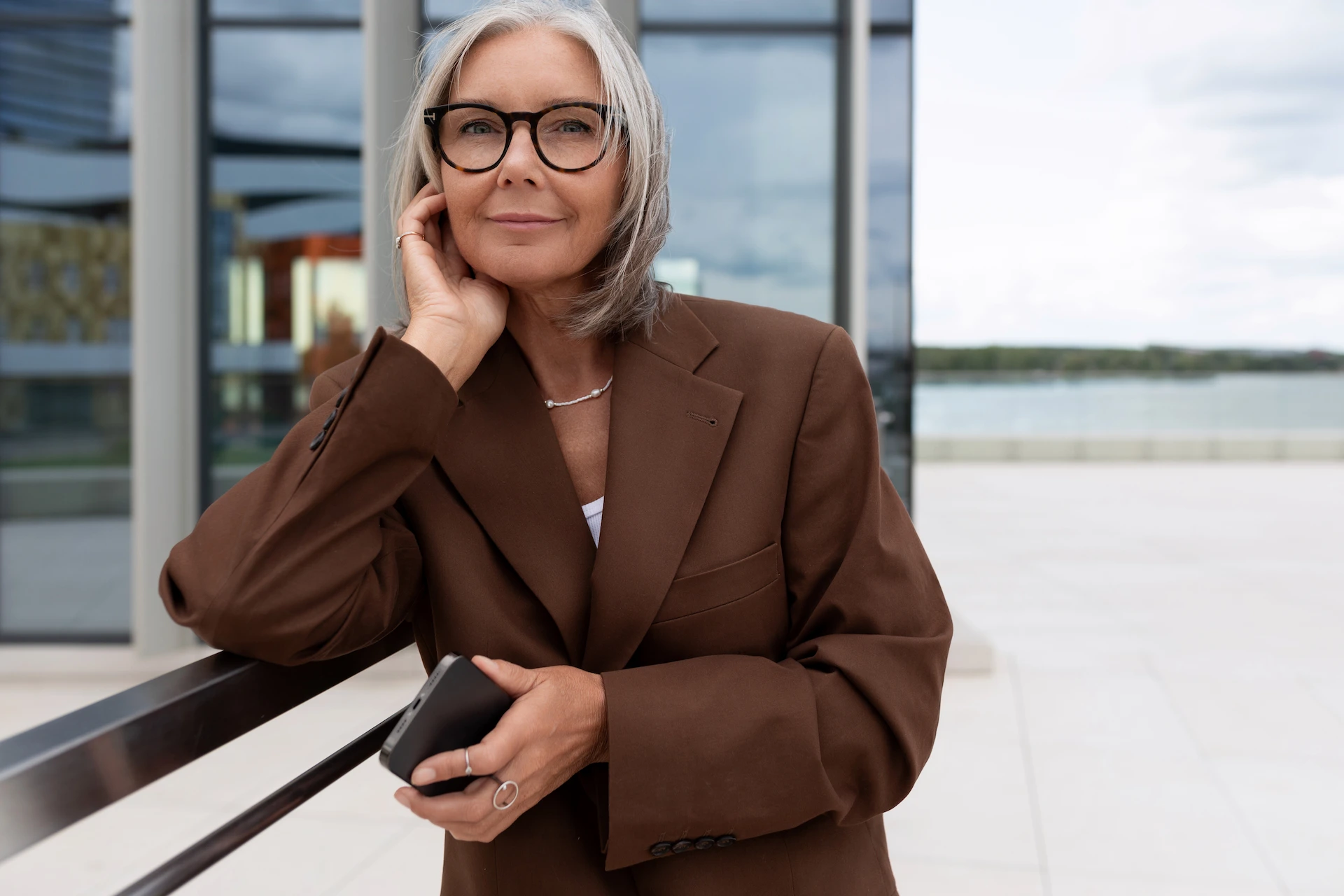 Woman in brown blazer leaning against a balcony railing.
