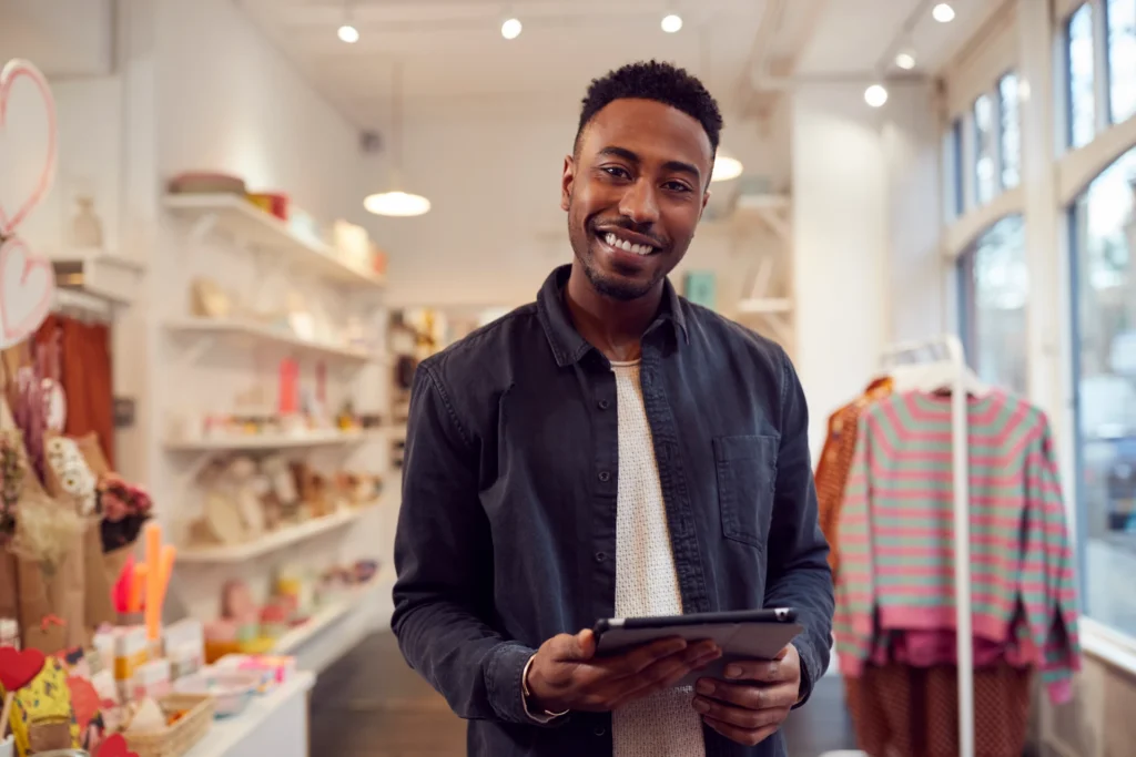Smiling small business owner holding a tablet in his clothing boutique.